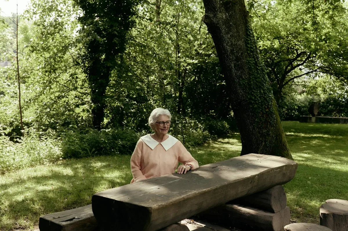 Man sieht eine ältere Dame an einem Tisch im Freien.